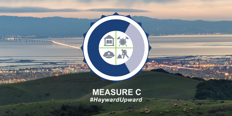 Photo of a vista of Hayward, the San Mateo bridge, and rolling green hills at sunset. On top is the Measure C logo.