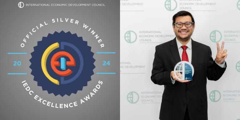 Chief Economic Development Officer, Paul Nguyen, standing with an IEDC award next to the IEDC Silver Award Winner banner