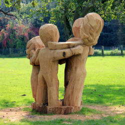 Large wooden sculpture of kids hugging in the middle of a park