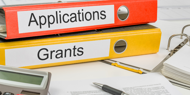 An orange and a yellow binder stacked with the text Applications and Grants