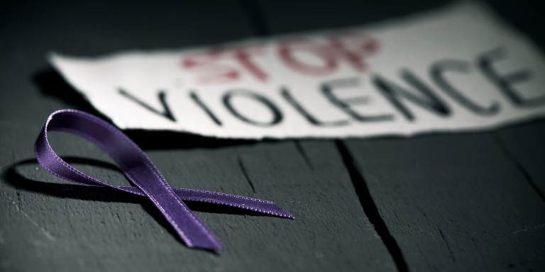 A purple domestic violence awareness ribbon next to a sign that says stop violence