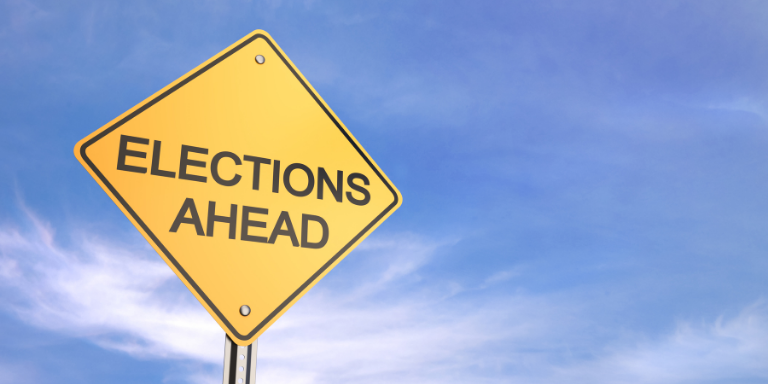 Yield sign with text "Elections Ahead" against a blue sky.