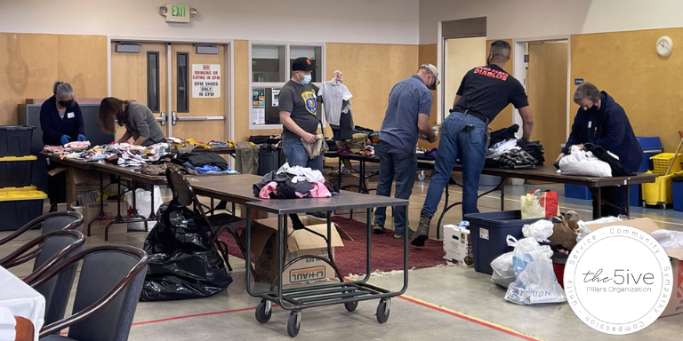 People organizing supplies and clothing on tables inside a gym.
