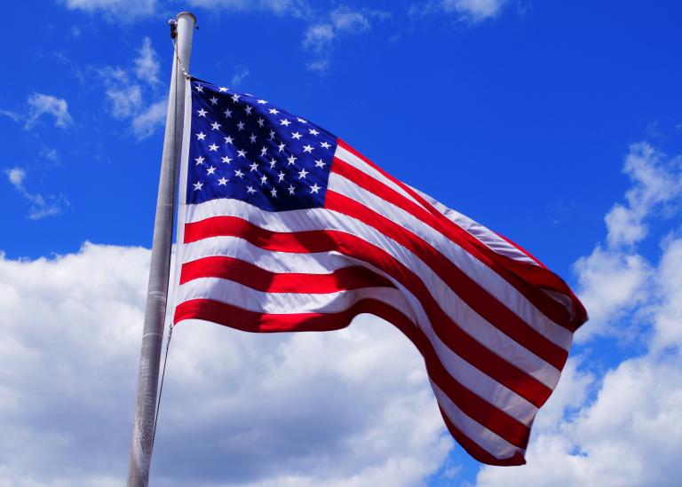 American flag against a bright blue sky with white cloud whisps