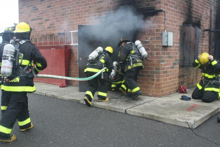 Fire fighter recruits in full turnout gear enter the training building with fire fighters