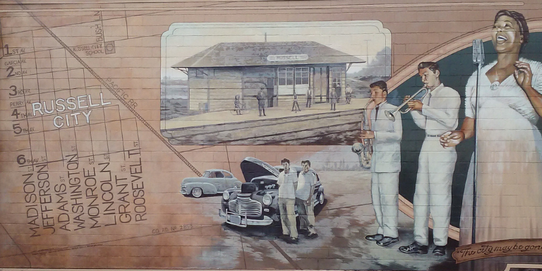 Photo of mural of Russell City depicting streets, train station, and a Black woman signing.