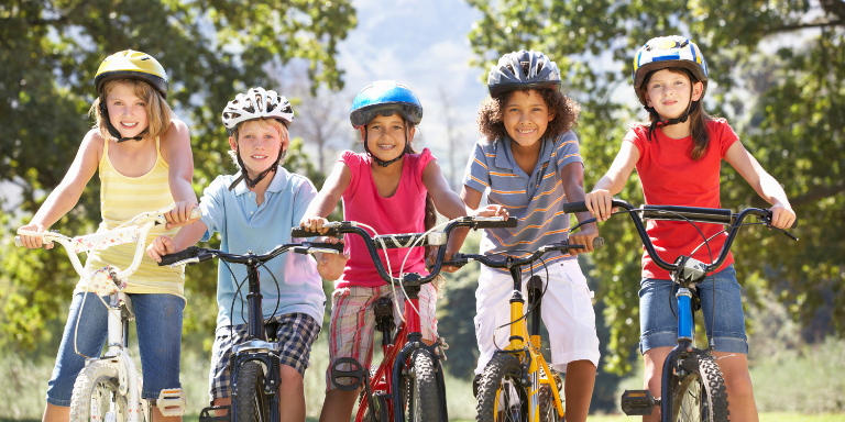 A group of children wearing helmets smiling on bikes