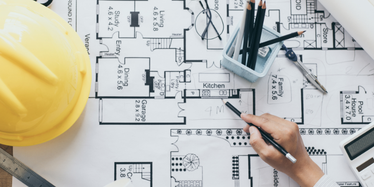 A person working on blueprints next to a yellow hard hat