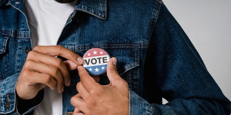 Photo of a person pinning a button that says "VOTE" to their denim jacket.