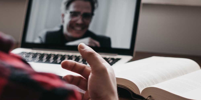 A person sitting with a book talking to someone on zoom