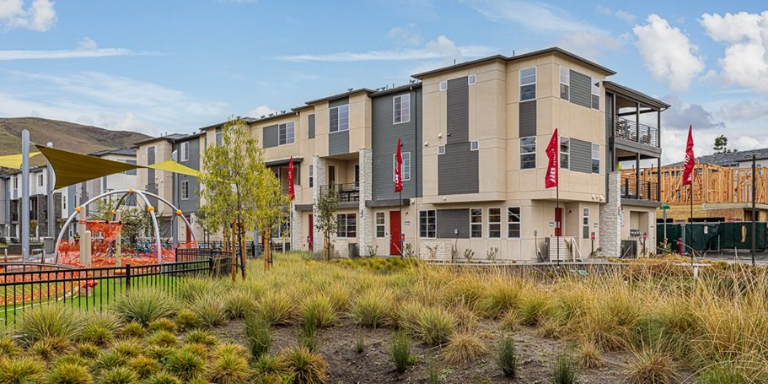 Photo of a grey and white apartment building behind a playground and drought-tolerant plant landscaping. 